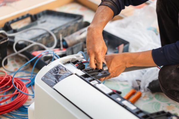 HVAC technician working on an outdoor air conditioning unit beside a home